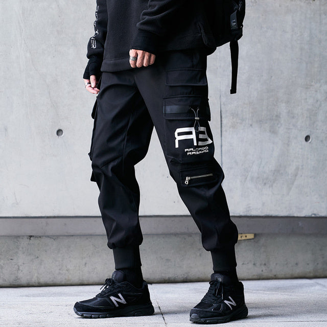 Black techwear joggers with patch detail, zippered pocket, and streetwear cargo styling

